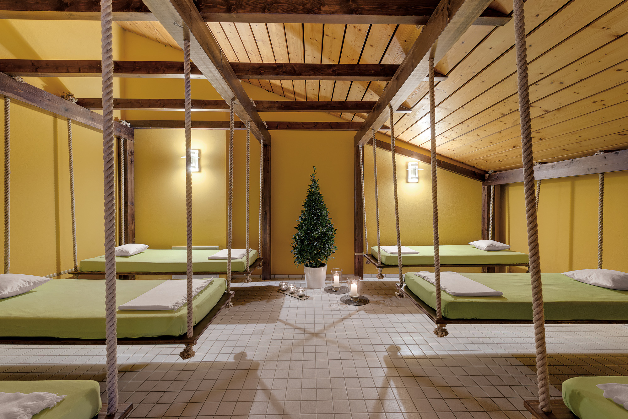 Holzraum mit grüner Bettwäsche auf mehreren Liegen, ruhige Atmosphäre und Pflanzen.