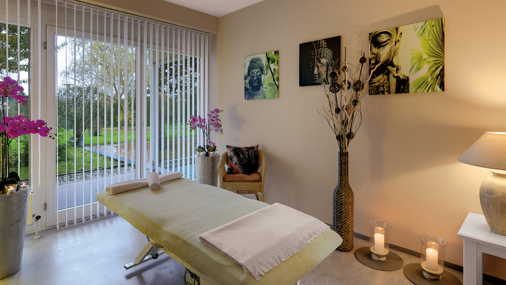  Massagezimmer mit Buddha-Bildern, Orchideen, Kerzen, Liege und beruhigendem Licht.