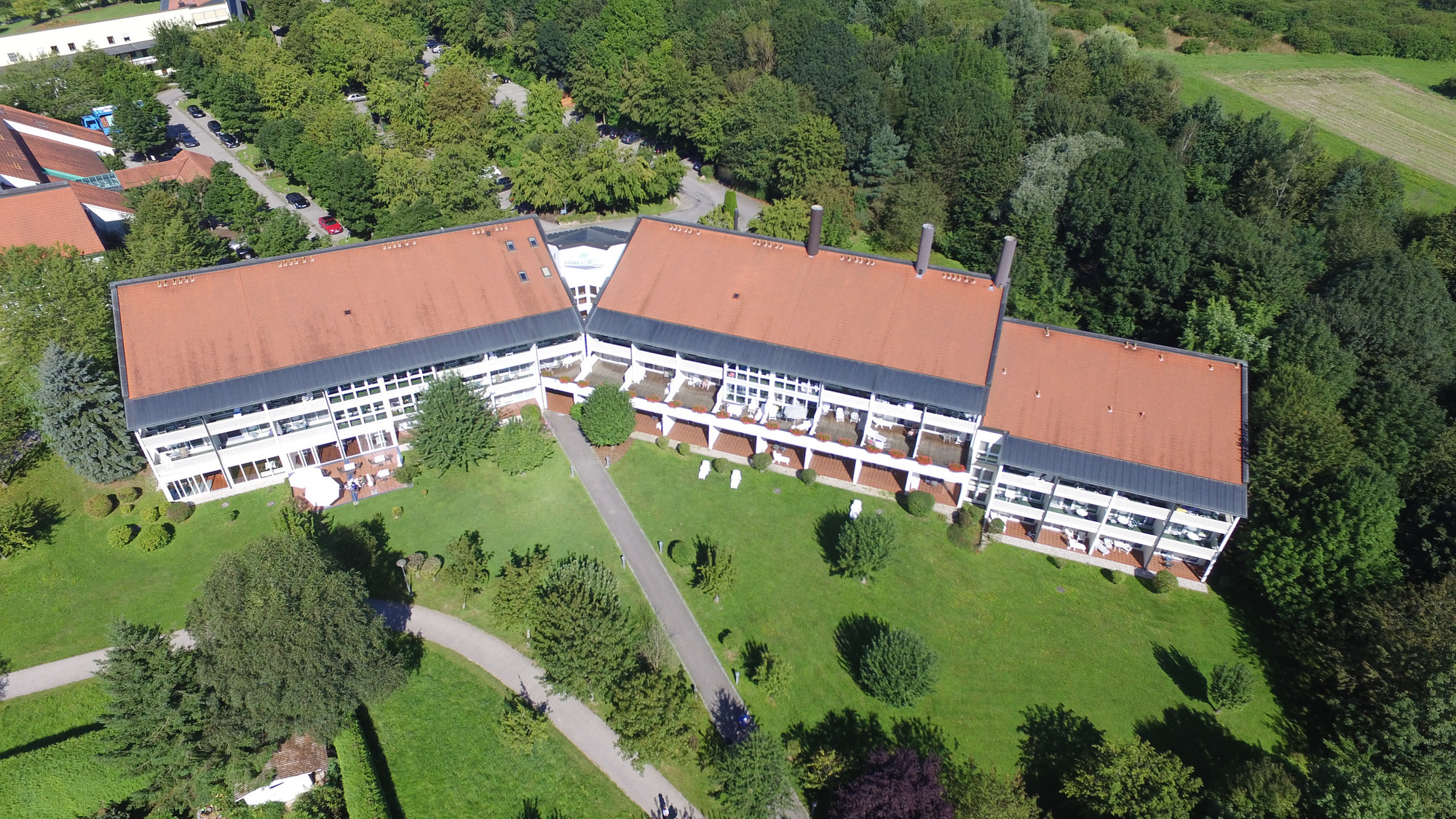 U-förmiges Gebäude mit Garten, Wegen, Bäumen und Rasen aus der Vogelperspektive