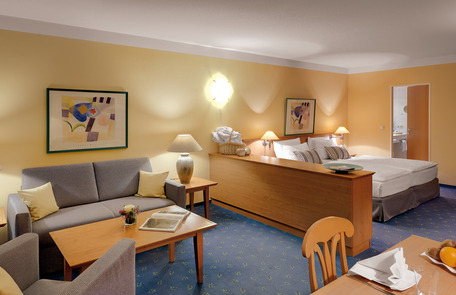 Großes Zimmer mit Bett, Sofa, Esstisch, gelben Wänden und gemütlicher Einrichtung