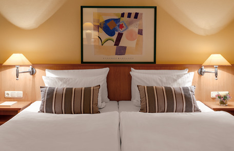 Zwei Einzelbetten mit weißer Bettwäsche, Holzmöbeln, Wandlampen und Blumen.